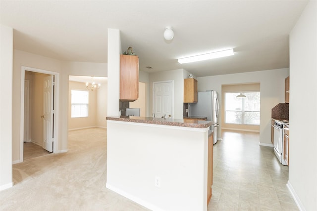 kitchen featuring stainless steel fridge, white range with gas cooktop, kitchen peninsula, and a healthy amount of sunlight