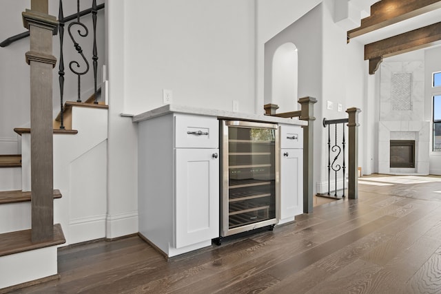 bar with wine cooler, dark hardwood / wood-style flooring, a tile fireplace, and white cabinets