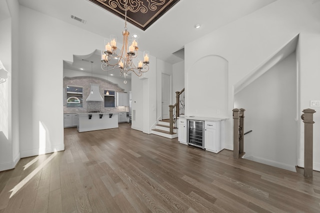 unfurnished living room with wood-type flooring, a towering ceiling, beverage cooler, and an inviting chandelier