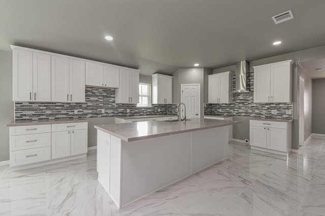 kitchen featuring sink, white cabinets, wall chimney range hood, and an island with sink