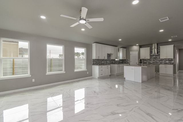 kitchen with sink, white cabinets, tasteful backsplash, wall chimney range hood, and a center island with sink