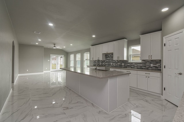 kitchen with light stone countertops, white cabinets, an island with sink, sink, and vaulted ceiling