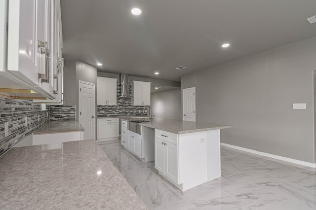 kitchen featuring light stone countertops, wall chimney exhaust hood, white cabinetry, sink, and a kitchen island with sink