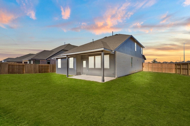 back house at dusk with a lawn and a patio