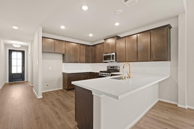 kitchen with sink, light wood-type flooring, dark brown cabinets, and appliances with stainless steel finishes