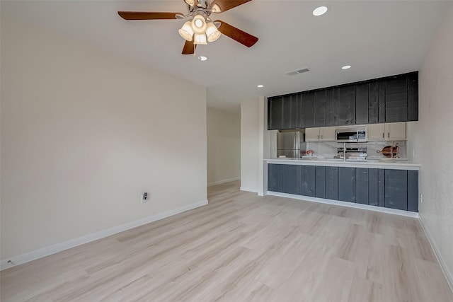 kitchen with light hardwood / wood-style floors, appliances with stainless steel finishes, decorative backsplash, kitchen peninsula, and ceiling fan