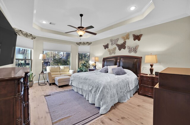 bedroom with ceiling fan, ornamental molding, a raised ceiling, and light hardwood / wood-style flooring