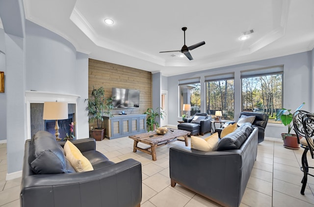 tiled living room with crown molding, ceiling fan, a tray ceiling, and wood walls