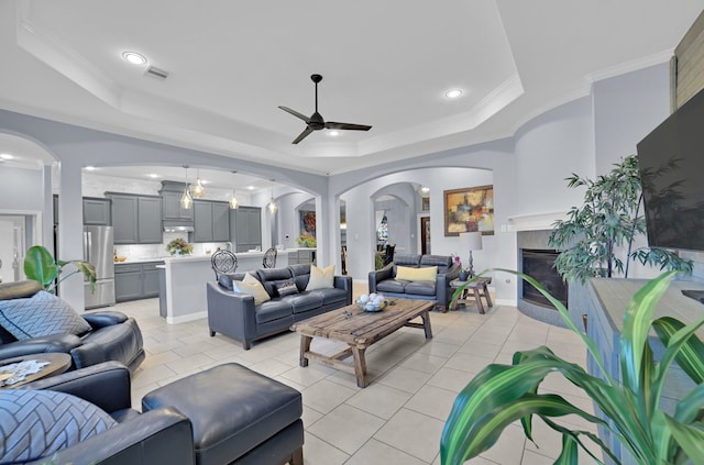 tiled living room with crown molding, a fireplace, a raised ceiling, and ceiling fan