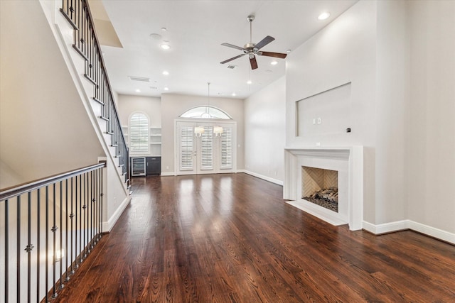 unfurnished living room featuring dark hardwood / wood-style flooring, ceiling fan with notable chandelier, and a high ceiling