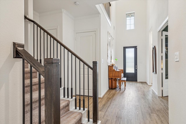 entrance foyer with light wood-type flooring, a high ceiling, and crown molding