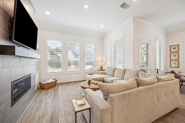 living room with ornamental molding, lofted ceiling, a tiled fireplace, and light wood-type flooring