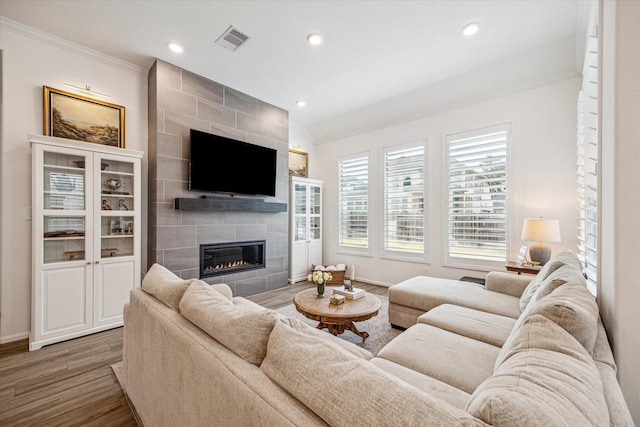 living room featuring wood-type flooring, a tiled fireplace, a healthy amount of sunlight, and ornamental molding