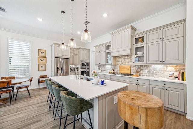 kitchen with pendant lighting, appliances with stainless steel finishes, a kitchen bar, tasteful backsplash, and a center island with sink