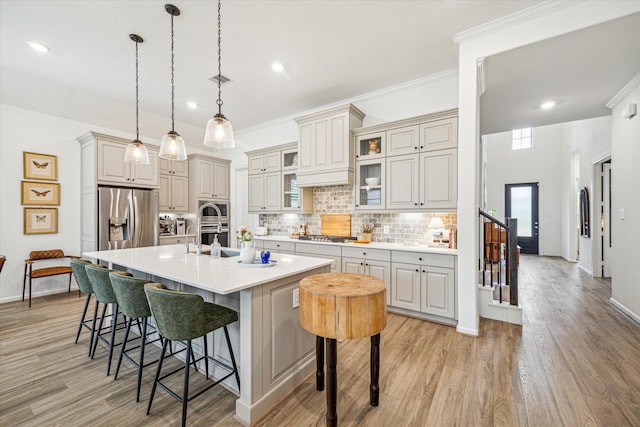 kitchen featuring a kitchen breakfast bar, hanging light fixtures, backsplash, an island with sink, and stainless steel appliances