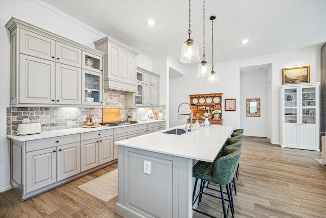 kitchen with stainless steel gas cooktop, a kitchen island with sink, decorative backsplash, a kitchen breakfast bar, and sink