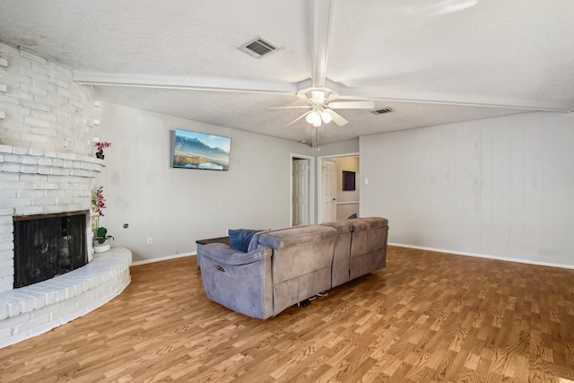 living room with a fireplace, light hardwood / wood-style floors, a textured ceiling, and beamed ceiling