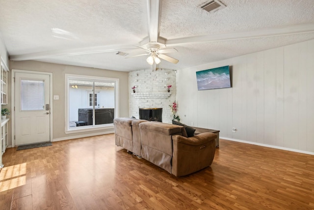 living room featuring ceiling fan, a brick fireplace, hardwood / wood-style floors, a textured ceiling, and wooden walls