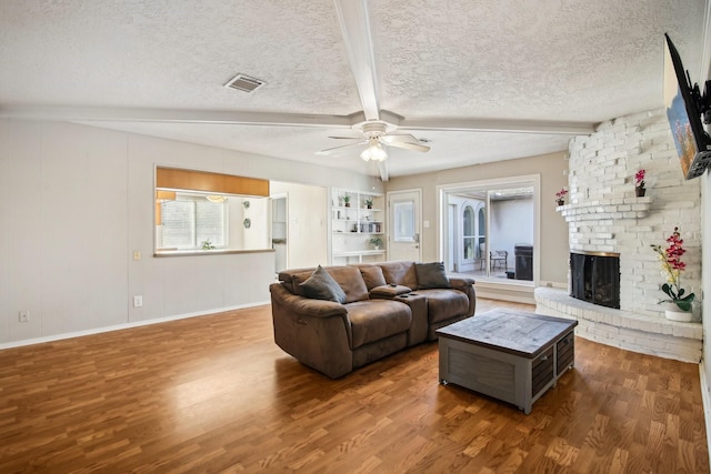 living room with a fireplace, dark wood-type flooring, a textured ceiling, and beamed ceiling