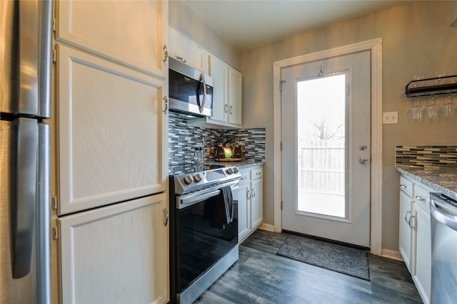 kitchen with appliances with stainless steel finishes, tasteful backsplash, dark stone countertops, white cabinets, and plenty of natural light