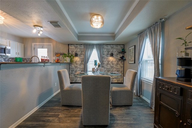 dining room featuring sink, a textured ceiling, ornamental molding, dark hardwood / wood-style flooring, and a raised ceiling