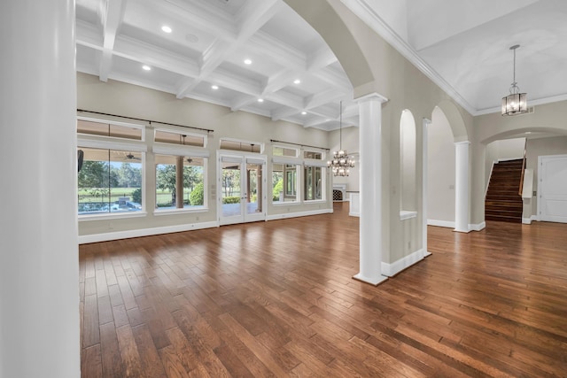 unfurnished living room with a towering ceiling, beamed ceiling, ornate columns, a chandelier, and dark hardwood / wood-style flooring