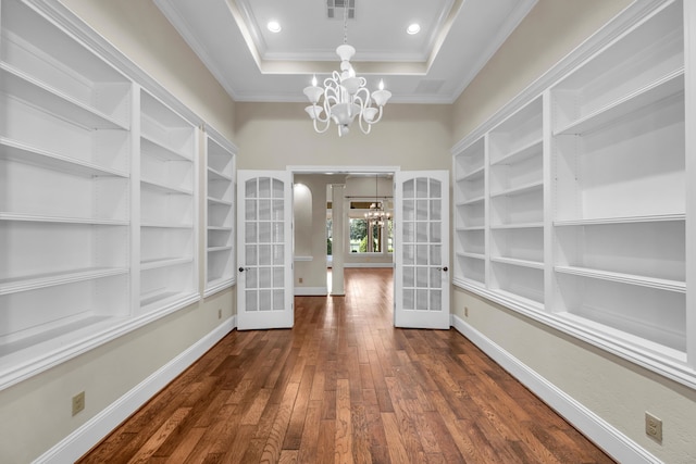 unfurnished dining area with french doors, ornamental molding, an inviting chandelier, dark wood-type flooring, and a tray ceiling