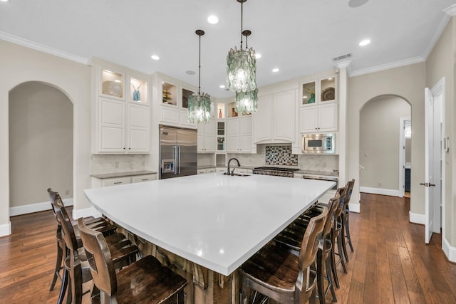 kitchen featuring built in appliances, a kitchen bar, a spacious island, hanging light fixtures, and decorative backsplash