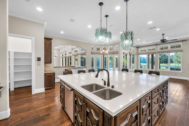 kitchen featuring pendant lighting, dark wood-type flooring, sink, a kitchen island with sink, and crown molding