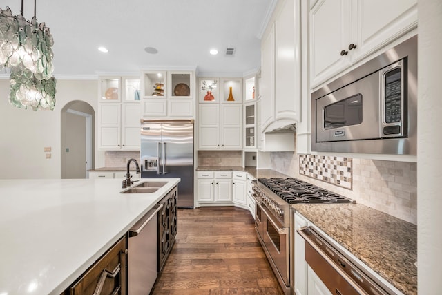 kitchen featuring pendant lighting, white cabinetry, built in appliances, sink, and ornamental molding