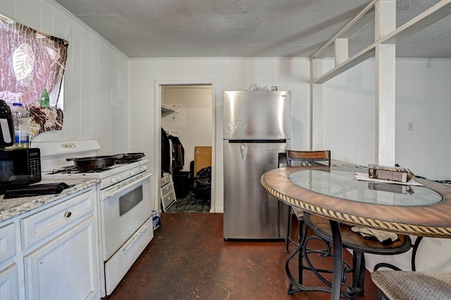 kitchen featuring a textured ceiling, white cabinets, white gas range, light stone counters, and stainless steel fridge