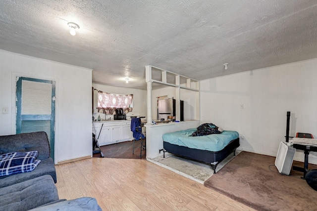 bedroom with light hardwood / wood-style floors, a textured ceiling, and stainless steel refrigerator