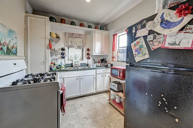 kitchen featuring sink, white range with gas cooktop, black refrigerator, and white cabinets