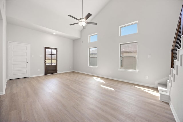 unfurnished living room with a towering ceiling, ceiling fan, and light hardwood / wood-style floors