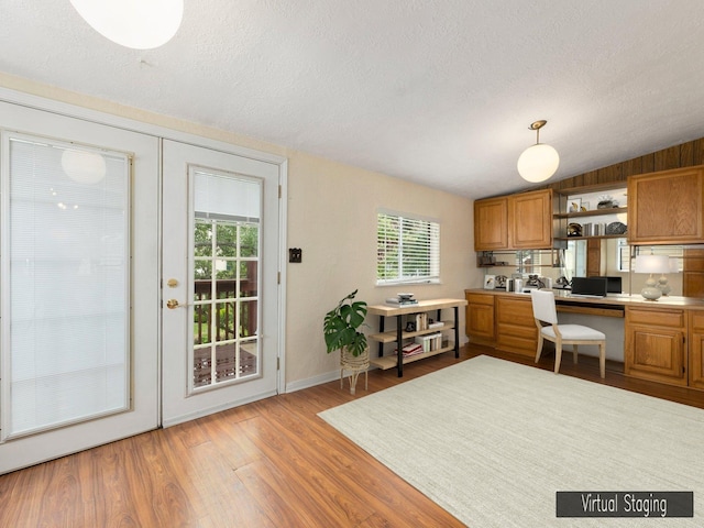 kitchen with pendant lighting, a textured ceiling, built in desk, french doors, and light hardwood / wood-style flooring