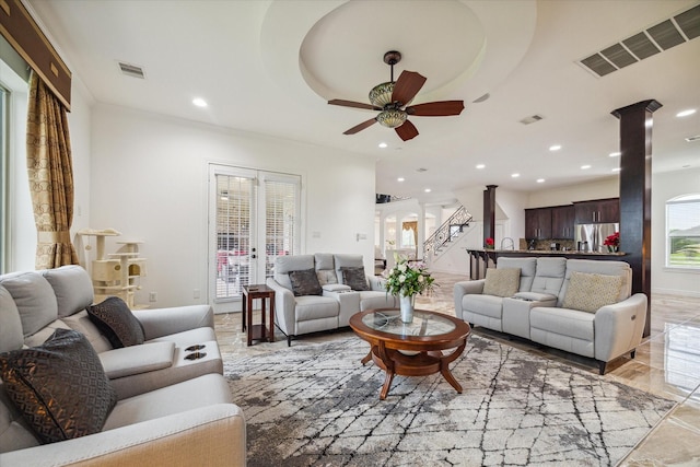 living room featuring ceiling fan, decorative columns, and a tray ceiling