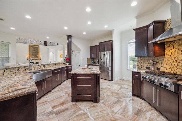 kitchen with wall chimney exhaust hood, a kitchen island, stainless steel appliances, decorative backsplash, and light stone counters