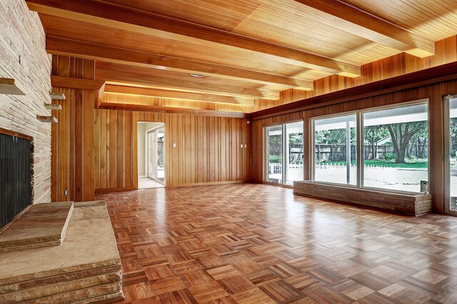 unfurnished living room with beamed ceiling, wooden walls, parquet floors, and a stone fireplace