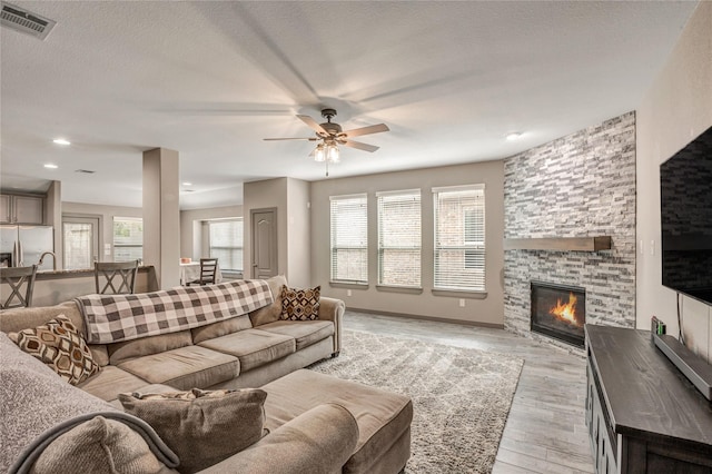 living room featuring ceiling fan, light hardwood / wood-style flooring, a fireplace, and a textured ceiling