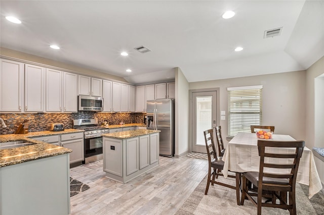 kitchen featuring appliances with stainless steel finishes, a center island, sink, light stone counters, and light hardwood / wood-style flooring