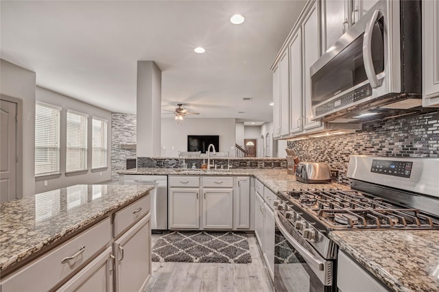 kitchen featuring stainless steel appliances, light hardwood / wood-style floors, decorative backsplash, ceiling fan, and light stone counters