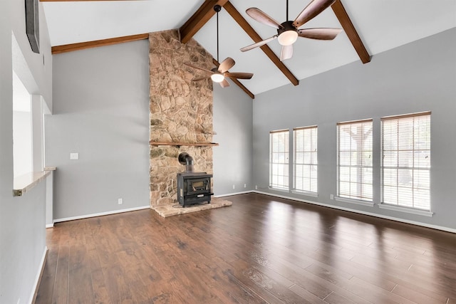 unfurnished living room with a wood stove, beamed ceiling, a wealth of natural light, and high vaulted ceiling