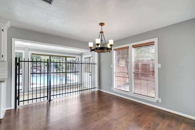 unfurnished dining area featuring a wealth of natural light, dark hardwood / wood-style floors, a textured ceiling, and a chandelier