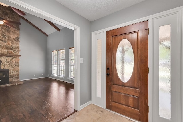 foyer entrance with light hardwood / wood-style flooring, a textured ceiling, vaulted ceiling with beams, and a wood stove