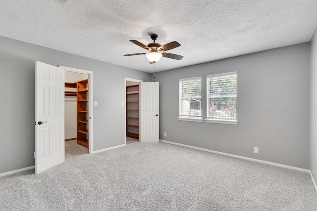 unfurnished bedroom with ceiling fan, light colored carpet, a textured ceiling, a spacious closet, and a closet