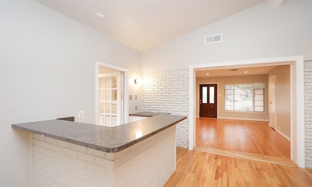 kitchen with kitchen peninsula, brick wall, hardwood / wood-style floors, and lofted ceiling