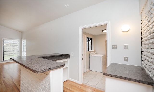 kitchen featuring kitchen peninsula, light hardwood / wood-style flooring, vaulted ceiling, a breakfast bar area, and washer and clothes dryer