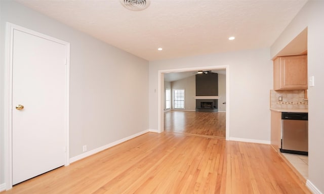 kitchen with light brown cabinetry, decorative backsplash, stainless steel dishwasher, and light hardwood / wood-style flooring