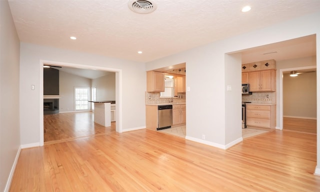 unfurnished living room with sink, light hardwood / wood-style floors, a textured ceiling, and vaulted ceiling