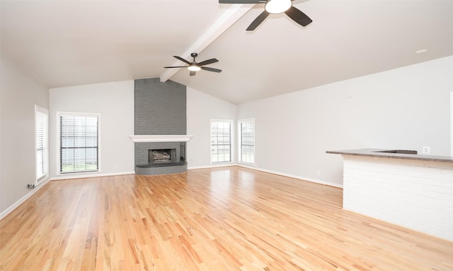 unfurnished living room featuring ceiling fan, light wood-type flooring, vaulted ceiling with beams, and a brick fireplace